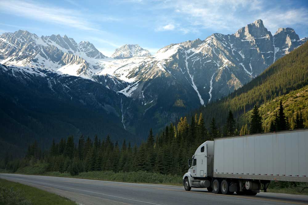 Semi truck driving scenic route with mountains in background after driver rehab